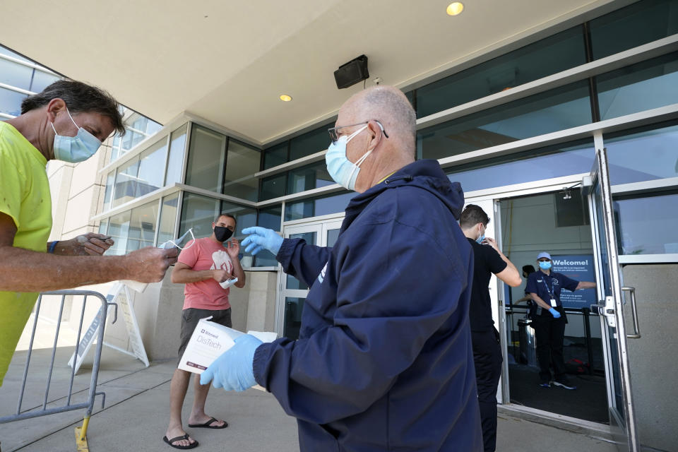 James Doyle, front right, hands out face masks as people arrive at a COVID-19 mass vaccination clinic, Wednesday, May 19, 2021, at Gillette Stadium, in Foxborough, Mass. A month after every adult in the U.S. became eligible for the vaccine, a distinct geographic pattern has emerged: The highest vaccination rates are concentrated in the Northeast, while the lowest ones are mostly in the South. (AP Photo/Steven Senne)