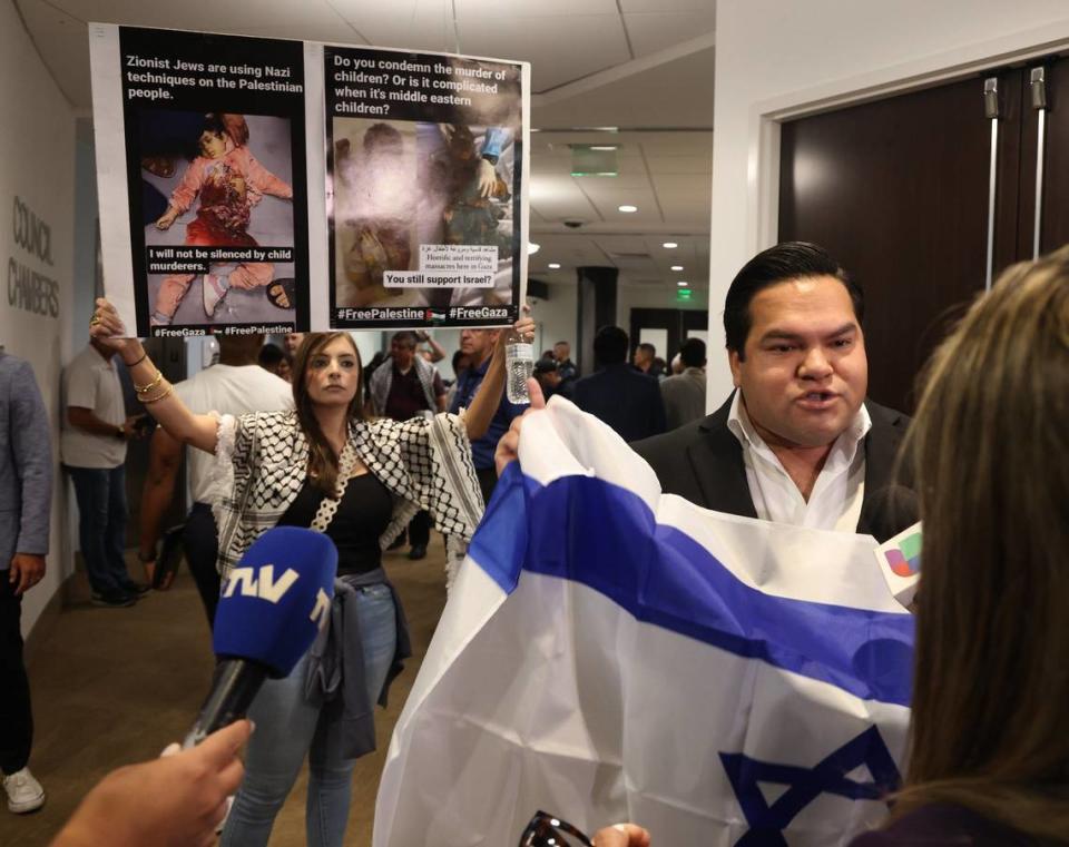 Sabren Najjar, left, holds pictures of dead Palestinian babies, as Samuel Aldana, speaks to the press after the special council meeting to rescind its Israel-Palestine peace resolution in the city of Doral.