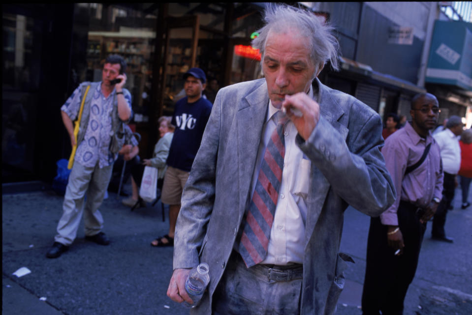 Não muito longe do World Trade Center, um homem que sobreviveu aos destroços das torres em chamas fuma um cigarro e uma garrafa de água, grato por estar vivo