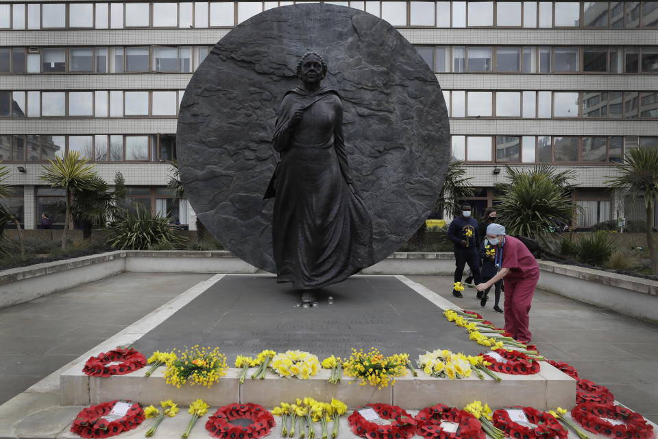 A member of NHS staff lays flowers under the Mary Seacole statue after a minute of silence and reflection at St Thomas' hospital in London, Tuesday, March 23, 2021. The U.K. has a lot to reflect on a year after British Prime Minister Boris Johnson first announced that the country would go into lockdown to slow the fast-spreading coronavirus. A national day of reflection taking place on Tuesday will remember more than 126,000 people who died after contracting the virus. (AP Photo/Kirsty Wigglesworth)