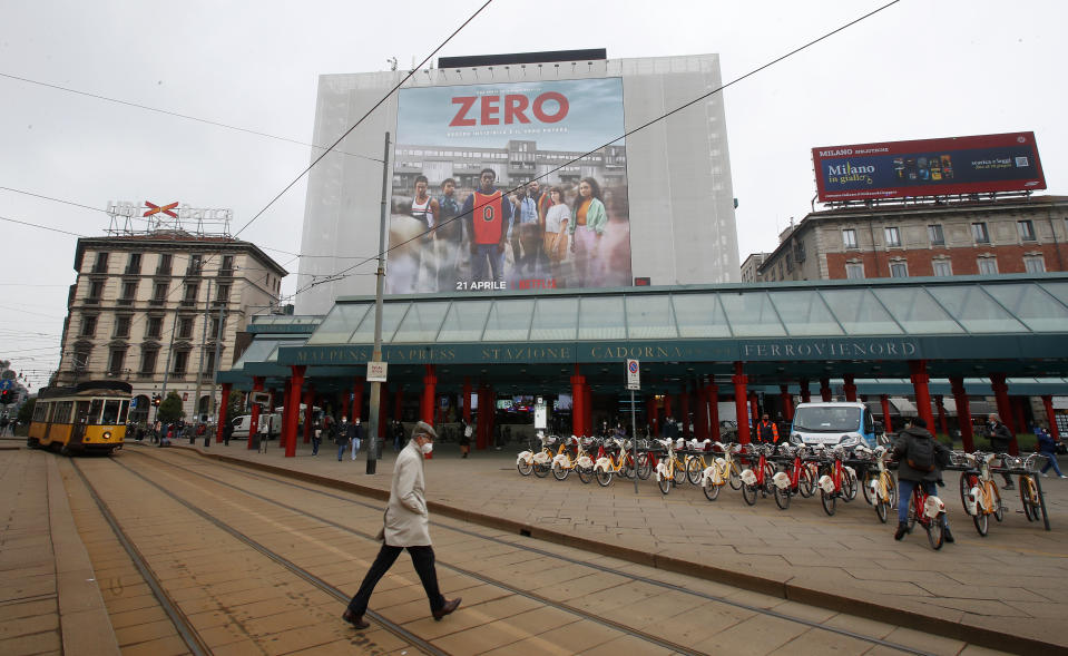 A man walks under a poster advertising the TV Series "Zero", at Cadorna square in Milan, Italy, Tuesday, April 27, 2021. The Netflix series “Zero,” which premiered globally last month, is the first Italian TV production to feature a predominantly black cast, a bright spot in an otherwise bleak television landscape where the persistent use of racist language and imagery in Italy is sparking new protests. (AP Photo/Antonio Calanni)