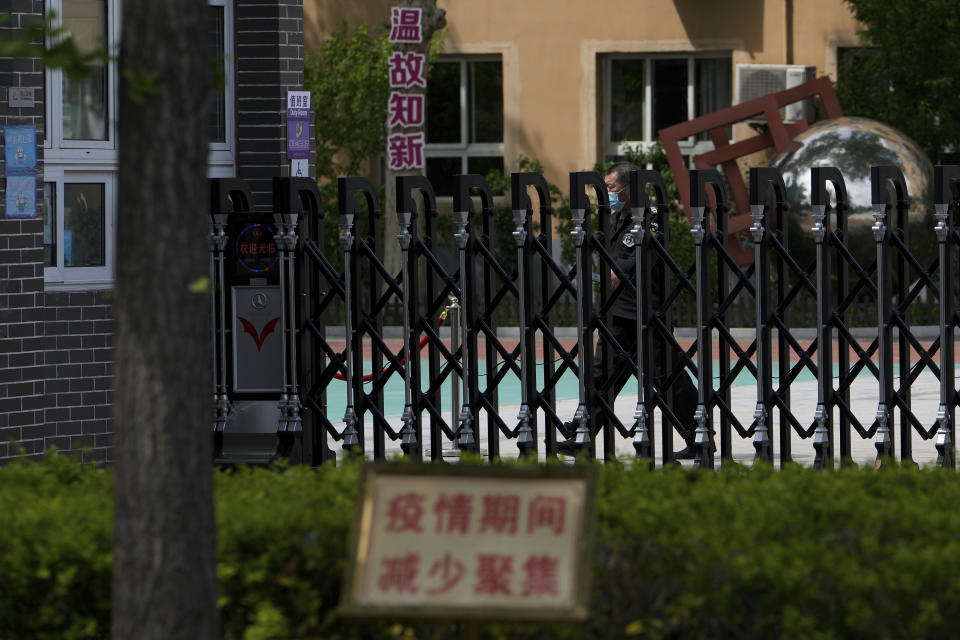 A security guard wearing a face mask walks inside the main entrance gate of a shuttered primary school in the Chaoyang district of Beijing, Thursday, April 28, 2022. Beijing shifted more classes online Thursday in a further tightening of COVID-19 restrictions, as China's capital seeks to prevent a wider outbreak. (AP Photo/Andy Wong)