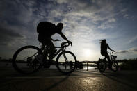 People wearing face masks to help curb the spread of the coronavirus are silhouetted as they ride bicycles near the Han River in Seoul, South Korea, Thursday, Sept. 23, 2021. (AP Photo/Lee Jin-man)