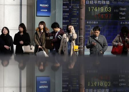 People standing in front of an electronic board showing the Japan's nikkei average outside a brokerage are reflected in a polished stone surface in Tokyo November 19, 2014. REUTERS/Yuya Shino