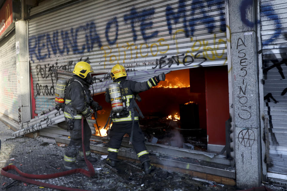 ADDS FIRE WAS STARTED BY PROTESTERS - Firefighters force open the bottom floor of a small shopping center that was set fire by anti-government protesters in Santiago, Chile, Monday, Oct. 28, 2019. Fresh protests and attacks on businesses erupted in Chile Monday despite President Sebastián Piñera's replacement of eight important Cabinet ministers with more centrist figures, and his attempts to assure the country that he had heard calls for greater equality and improved social services.(AP Photo/Rodrigo Abd)