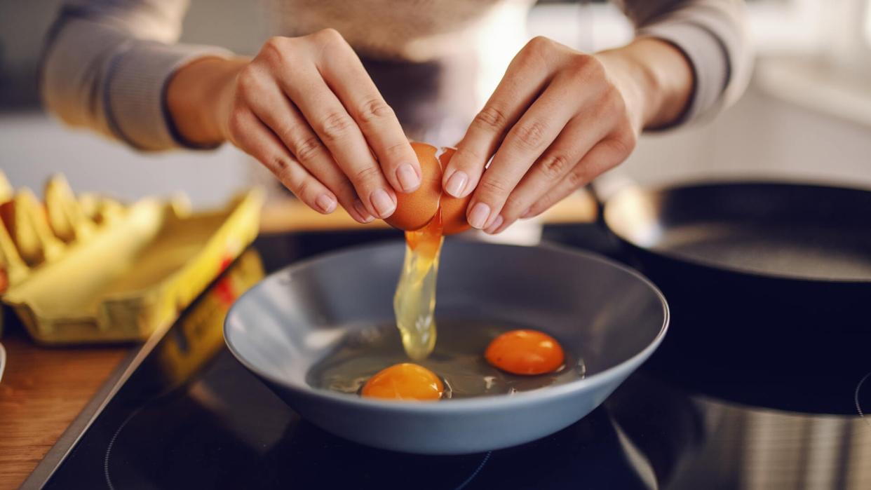 Close up of caucasian woman breaking egg and making sunny side up eggs.