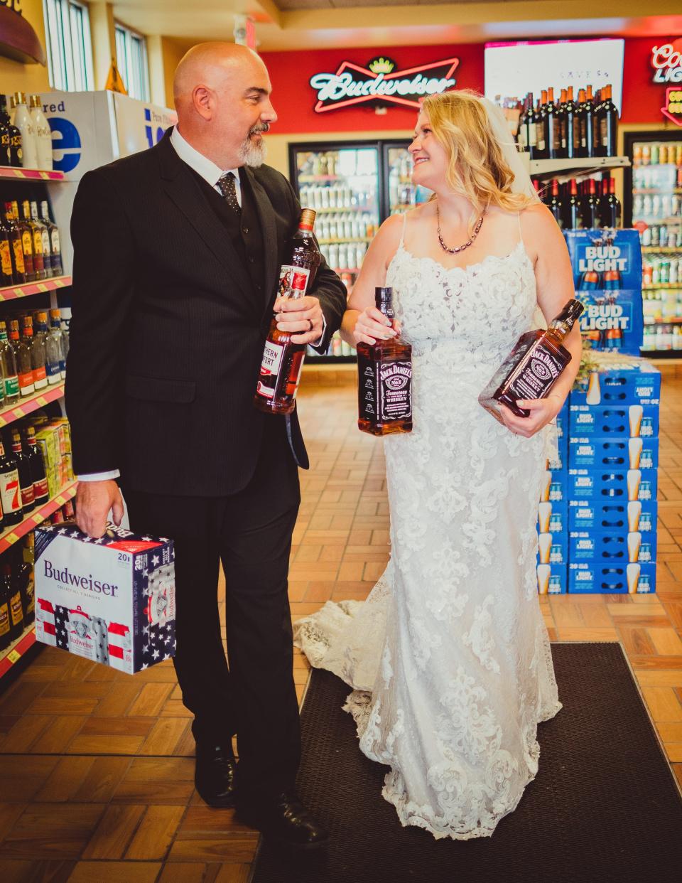 A bride and groom hold bottles of whiskey and beer.