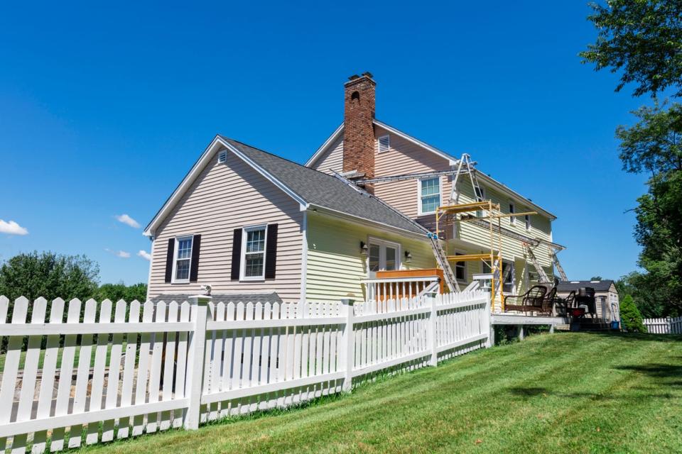 large house on green lawn with one side painted beige and the other yellow with scaffolding