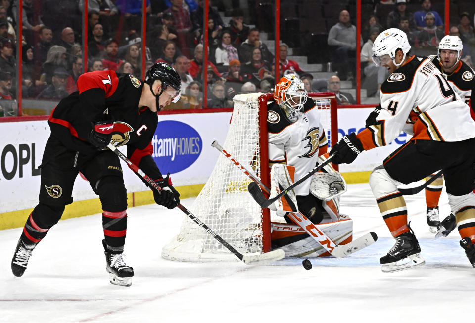 Ottawa Senators left wing Brady Tkachuk (7) tries to wrap the puck around the net of Anaheim Ducks goaltender Lukas Dostal, center, as Ducks defenseman Cam Fowler (4) defends during second-period NHL hockey game action in Ottawa, Ontario, Monday, Dec. 12, 2022. (Justin Tang/The Canadian Press via AP)