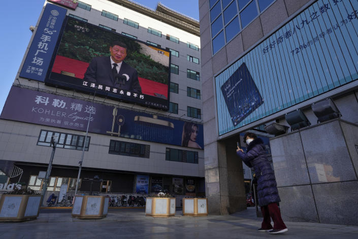 A woman films an outdoor screen showing a live broadcast of the memorial service for late former Chinese President Jiang Zemin where Chinese President Xi Jinping makes a speech at the Wangfujing shopping street in Beijing, Tuesday, Dec. 6, 2022. A formal memorial service was held Tuesday at the Great Hall of the People, the seat of the ceremonial legislature in the center of Beijing. (AP Photo/Andy Wong)