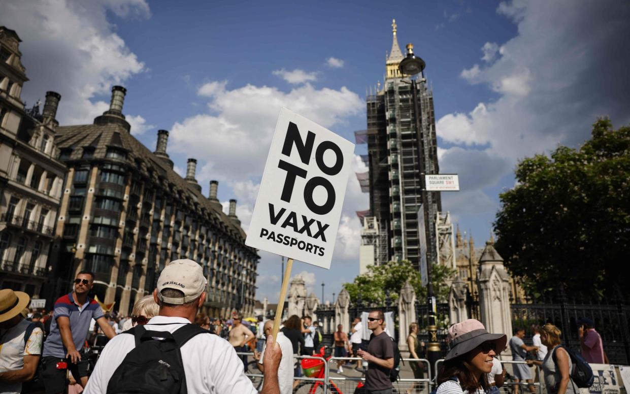 Anti-vaccination protesters, including one holding a placard against coronavirus vaccine passports, gather in Parliament Square outside the Houses of Parliament - Tolga Akmen/AFP