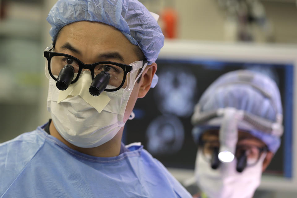 In this Jan. 14, 2020 photo, neurosurgeon Dr. Andrew Ko, left, of the University of Washington School of Medicine, wears glasses with magnifying lenses in the operating room as he works with senior resident Dr. Ariana Barkley, right, to perform brain surgery on Genette Hofmann at Harborview Medical Center in Seattle in hopes of reducing the epileptic seizures that had disrupted Hofmann's life for decades. At the same time, Hofmann agreed to donate a small bit of her healthy brain tissue to researchers, who were eager to study brain cells while they were still alive. (AP Photo/Ted S. Warren)