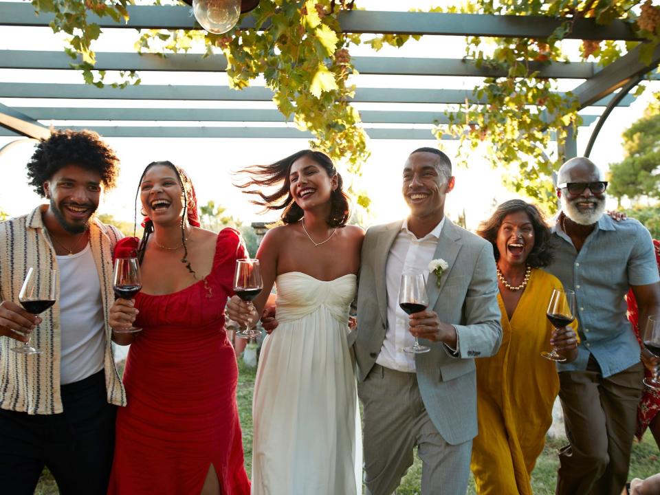 A bride, groom, and their wedding guests raise glasses of wine at their wedding.