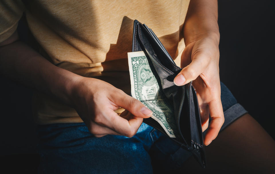 Person sitting down and removing a $1 bill from a wallet