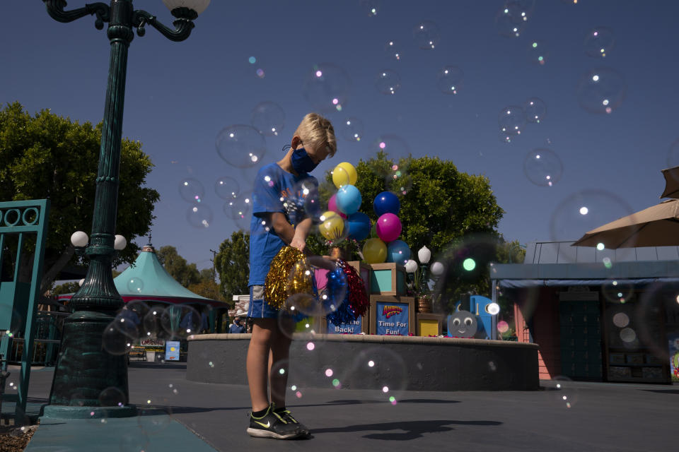 Luke Walker, 9, a grandnephew of Allan Ansdell Jr., owner and president of Adventure City amusement park, holds pompoms near the entrance to welcome visitors on the day of reopening at the amusement park in Anaheim, Calif., Friday, April 16, 2021. The family-run amusement park that had been shut since March last year because of the coronavirus pandemic reopened on April 16. (AP Photo/Jae C. Hong)