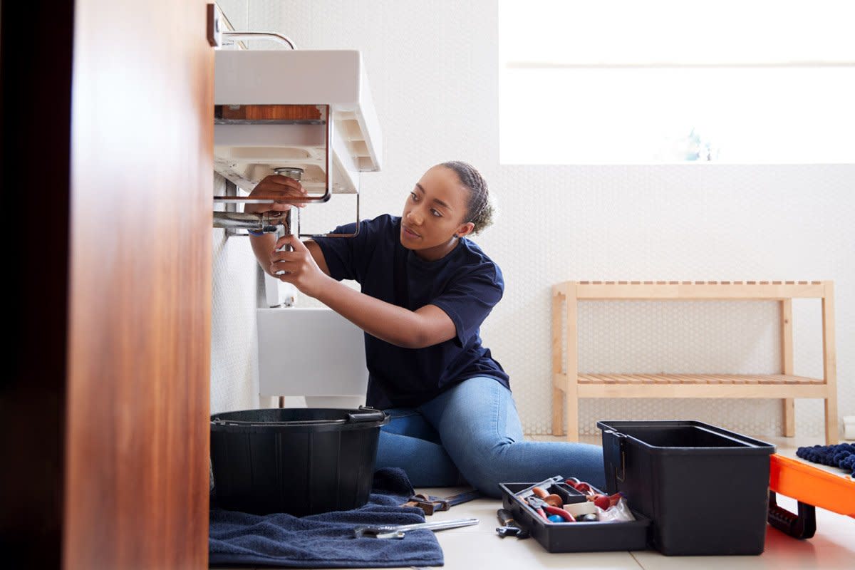 A woman checks pipes in a bathroom. 