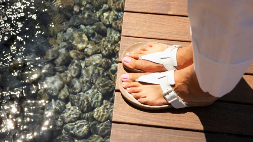 woman with sweaty feet wearing sandals while standing on a dock over the water