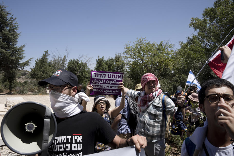 Israelis stand near the grave of Baruch Goldstein, a Jewish extremist who massacred 29 Muslim worshippers at Hebron's Ibrahimi Mosque in 1994, protest near the home of far-right National Security Minister Itamar Ben Gvir against plans by Benjamin Netanyahu's government efforts to overhaul the judiciary, in the West Bank settlement of Kiryat Arba, Friday, Aug. 25, 2023. (AP Photo/Maya Alleruzzo)