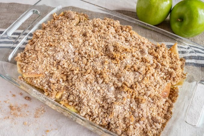 apple crisp topping sprinkled over sliced apples in a glass baking dish for pioneer woman apple crisp