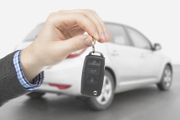 Male holding car keys with car on background