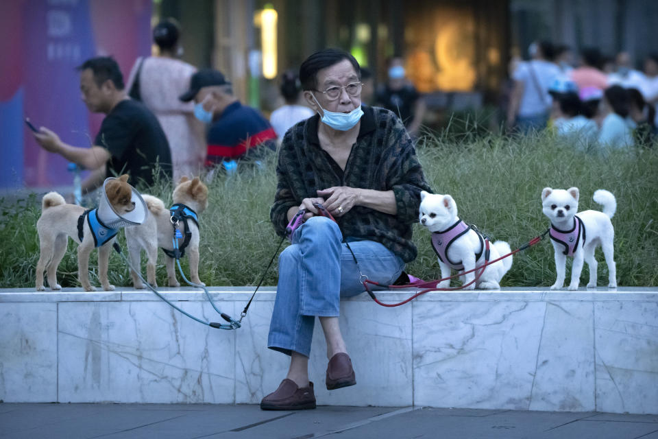 A man wearing a face mask to protect against COVID-19 sits with dogs on leashes near a neighborhood with a suspected coronavirus case in Beijing, Wednesday, Sept. 15, 2021. China tightened lockdowns and increased orders for mass testing in cities along its east coast Wednesday amid the latest surge in COVID-19 cases. (AP Photo/Mark Schiefelbein)