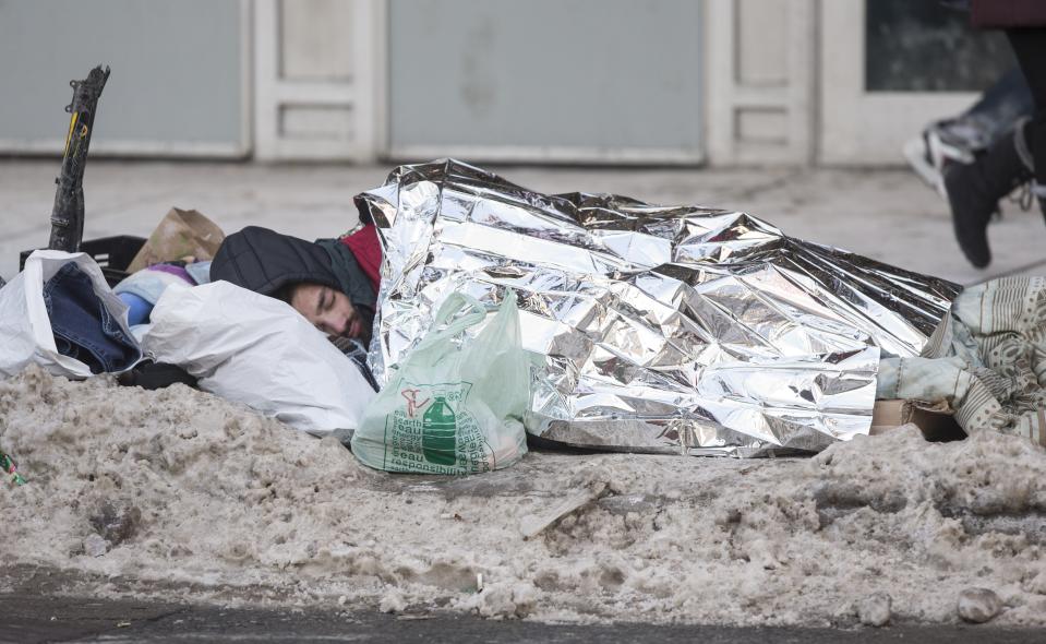 A homeless man sleeps under an emergency blanket on Dundas St. as pedestrians brave the cold at Dundas Square, Toronto. (Bernard Weil/Toronto Star via Getty Images)