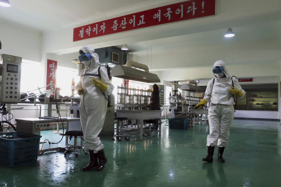 FILE- Health officials of the Pyongyang Sports Goods Factory disinfect the floor of a work place in Pyongyang, North Korea on June 14, 2022. The red banner says "Economy means increased production and patriotism." Only a month after North Korea acknowledged a COVID-19 outbreak was sickening its people, the country may be preparing to declare victory. The daily updates from state-controlled media say cases are plummeting. Its propaganda insists North Korea has avoided mass deaths despite desperately poor health care and what outsiders see as a long record of ignoring its people’s suffering. (AP Photo/Cha Song Ho, File)