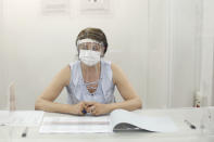 A woman wearing a face mask and visor to protect against coronavirus sits behind a glass shield during a rehearsal of the vote for the local elections scheduled for Sunday, June 28, in Paris, Friday, June 26, 2020. France is to hold its Covid-19 delayed second round of local elections on June 28. (AP Photo/Thibault Camus)