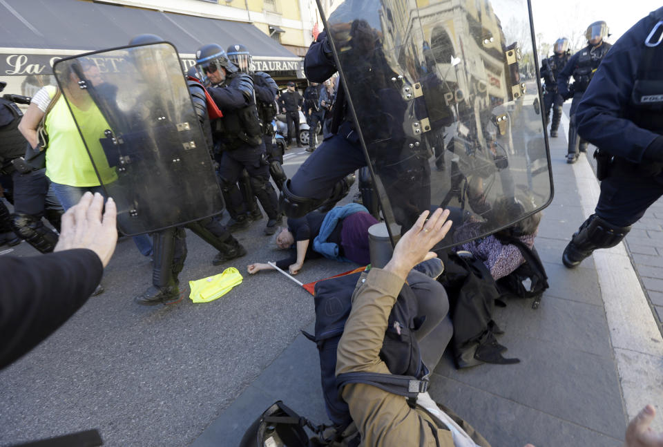 FILE - In this Saturday, March 23, 2019 file picture, anti-globalization activist Genevieve Legay, 73, center, lies unconscious after collapsing on the ground during a protest in Nice, southeastern France, as part of the 19th round of the yellow vests movement. Genevieve Legay was waving a rainbow flag marked "Peace" and a yellow vest when riot police carrying shields suddenly pushed toward the group of a few dozen protesters Saturday. (AP Photo/Claude Paris, File)