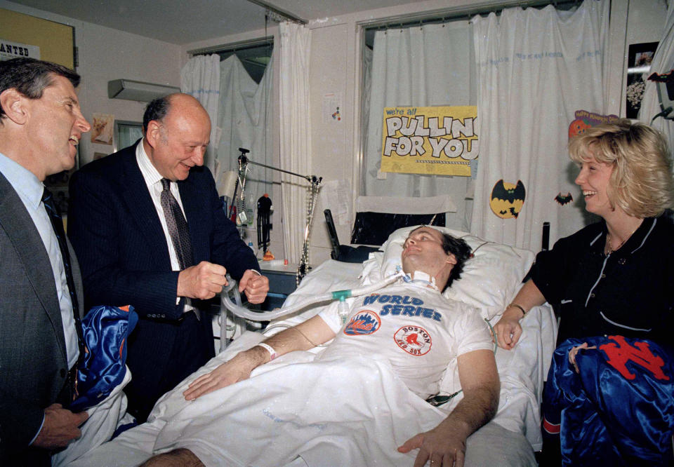 FILE - In this Oct. 30, 1986 file photo, NYPD Officer Steven McDonald, paralyzed after being shot in Central Park earlier in the year, receives a New York Mets baseball jacket from Mets' president Fred Wilpon, left, in McDonald's room in New York's Bellevue Hospital. They are jointed by then Mayor Ed Koch, second from left, and McDonald's wife Patti. McDonald, who was paralyzed by a bullet and became an international voice for peace after he publicly forgave the gunman, died Tuesday, Jan. 10, 2017 at the age of 59. (AP Photo/Mario Suriani, File)