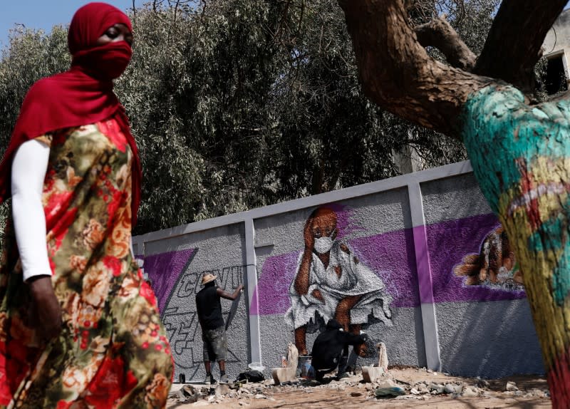 A woman walks past graffiti artists from RBS crew as they work on their mural to encourage people to protect themselves amid the outbreak of the coronavirus disease (COVID-19), in Dakar