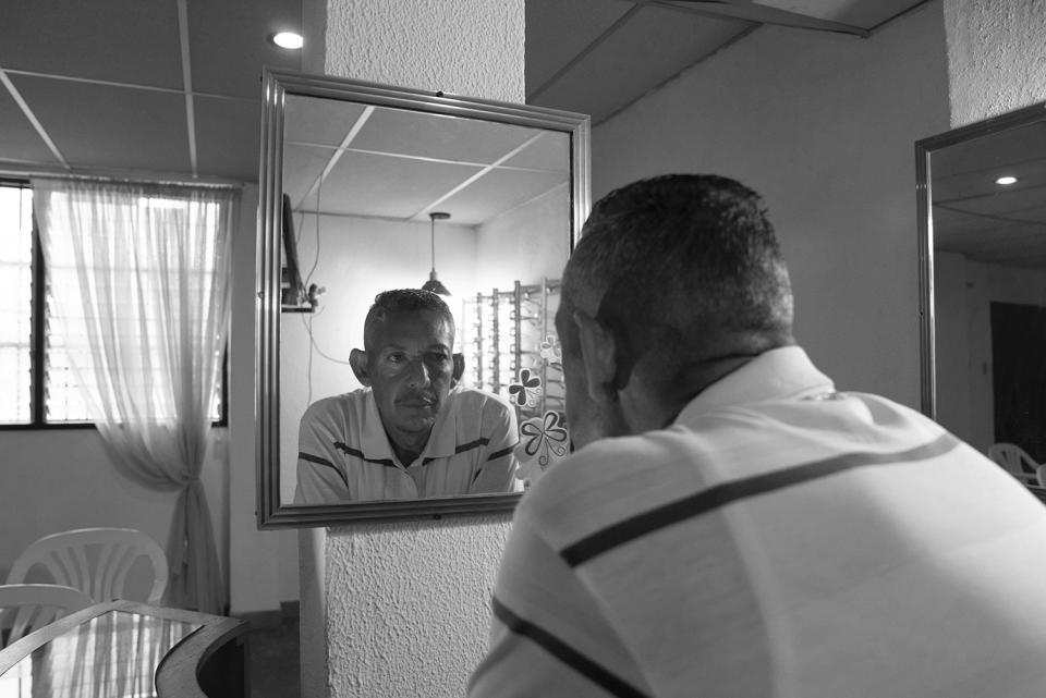 HOLD FOR DARIO LOPEZ -Jorge Montaño looks at himself in a mirror as he poses for a portrait at the office where he works repairing glasses and assisting an optomatrist in Caracas, Venezuela, Thursday, Feb. 23, 2023. Montaño, 51, who lives with his mother and three siblings at an apartment in Caracas. (AP Photo/Ariana Cubillos)