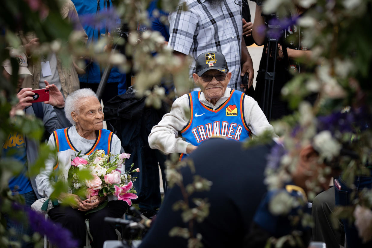 Viola Fletcher, left, holding a bunch of pink lilies, seated next to Hughes Van Ellis, wearing a blue vest saying: Thunder.                                                                                                                        and Hughes Van Ellis, both seated, attend a soil dedication ceremony for victims of the 1921 Tulsa Massacre in Tulsa, Oklahoma, U.S., on Monday, May 31, 2021. (Photo credit: Christian Monterrosa/Bloomberg)