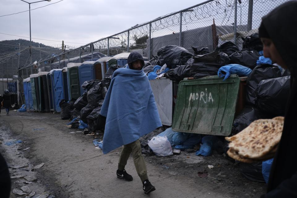 A migrant covered with a blanket passes in front of dumped garbage outside the Moria refugee camp on the northeastern Aegean island of Lesbos, Greece, on Tuesday, Jan. 21, 2020. Some businesses and public services on the eastern Aegean island are holding a 24-hour strike on Wednesday to protest the migration situation, with thousands of migrants and refugees are stranded in overcrowded camps in increasingly precarious conditions.(AP Photo/Aggelos Barai)