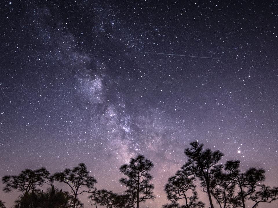 An outdoor shot shows a shooting star against the milky way in the sky.