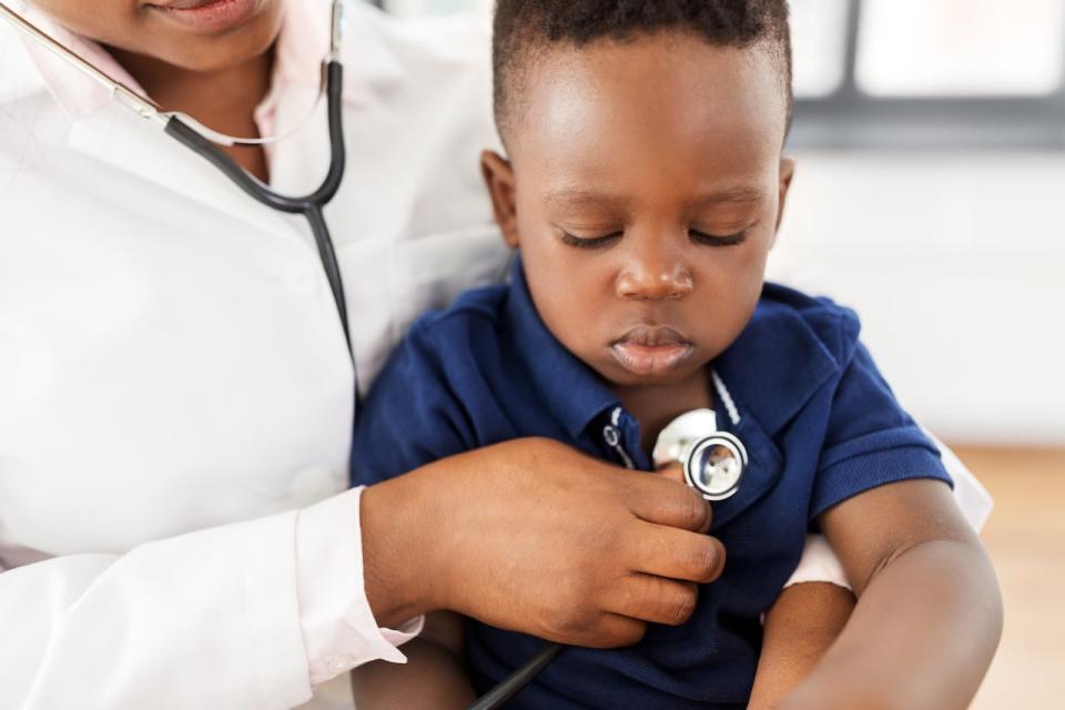 A stock photo shows a doctor holding a stethoscope to the chest of a toddler.