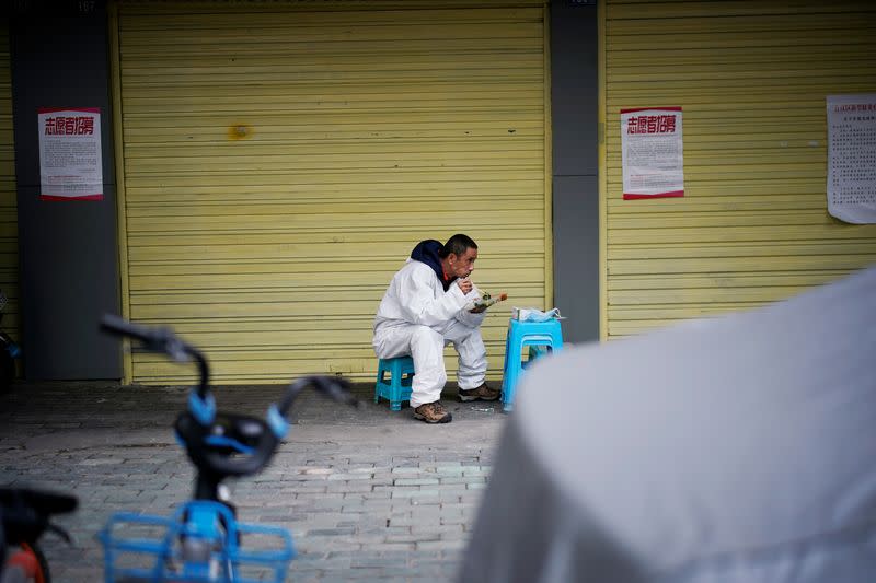 A man wearing a protective suit eats lunch on a street in Wuhan