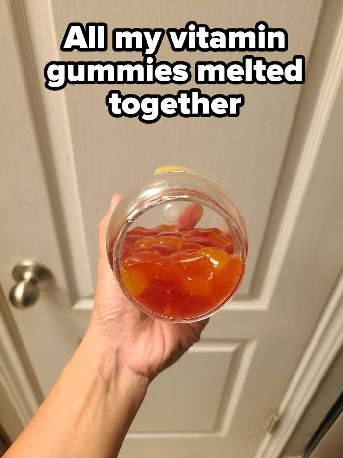 A hand holding a jar filled with orange gummy candies, viewed from above against a white door background