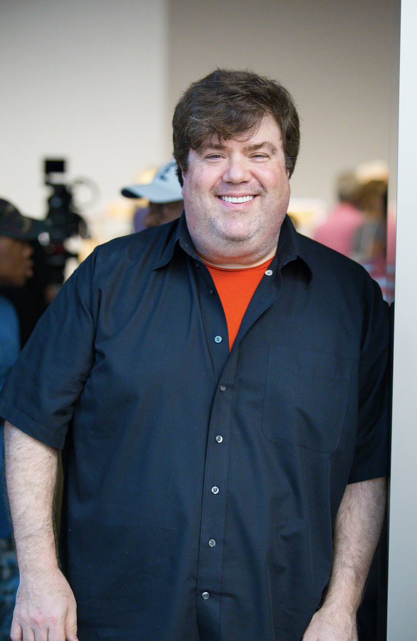 Dan Schneider smiles as he leans against a doorway