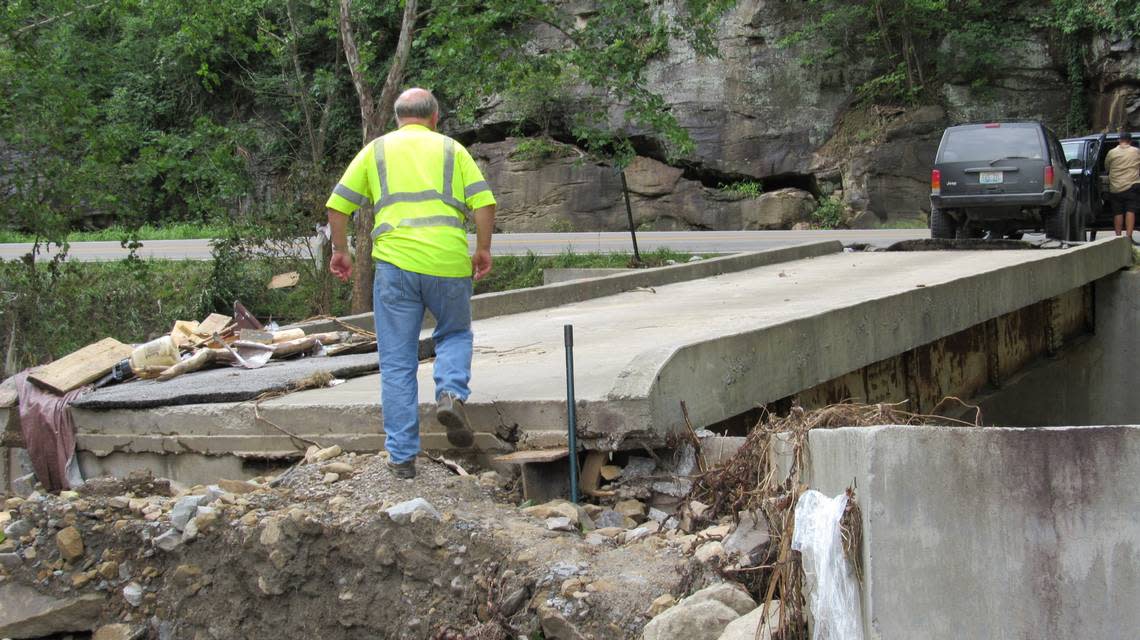 Flooding badly damaged a bridge in Perry County, Ky. Here, James Estep, whose house is served by the bridge, climbs across the end of the structure that was washed out to walk to his truck parked at the other end on Aug. 1, 2022.