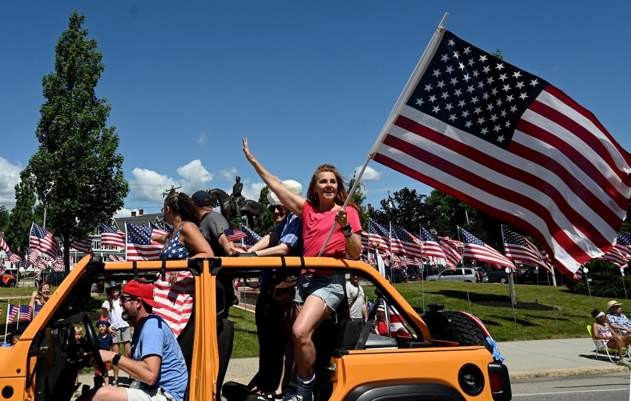 Molly Auger waves the American flag as the Jeep in which she's riding travels past Draper Park during the third annual Milford Fourth of July parade, July 4, 2022. Parades were held in Milford in 2018 and 2019 before a two-year hiatus due to the coronavirus pandemic.