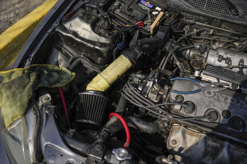 A PVC pipe is used to connect an air filter of an engine of a car being repaired on the side of the road that connects La Guaira with Caracas, Venezuela, Tuesday, April 19, 2022. Some Venezuelans have turned to YouTube for instruction on fixing their own cars. (AP Photo/Matias Delacroix)