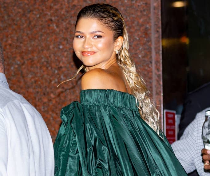 Zendaya wearing an off-the-shoulder, green, voluminous dress, smiling and glancing back over her shoulder while walking