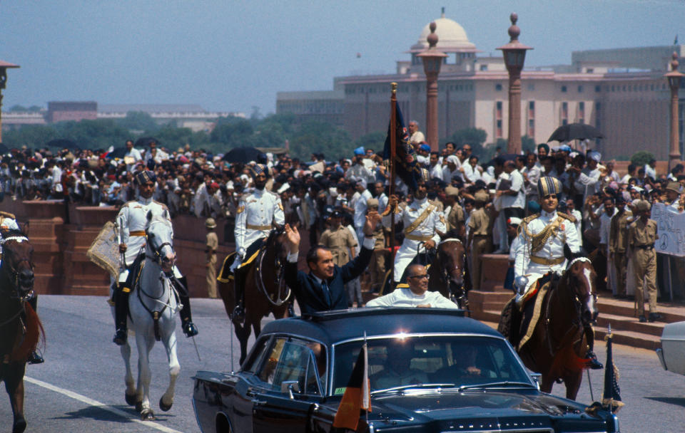 U.S. President Richard Nixon waves to crowds as he rides in open car with the acting president of India, Mohammad Hidyatullah, in motorcade from airport on July 31, 1969. | Bettmann Archive/Getty Images