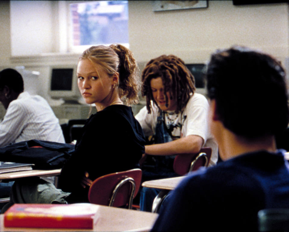 Julia Stiles sits in a high school classroom desk, glaring over her shoulder at Andrew Keegan in a scene from "10 Things I Hate About You"