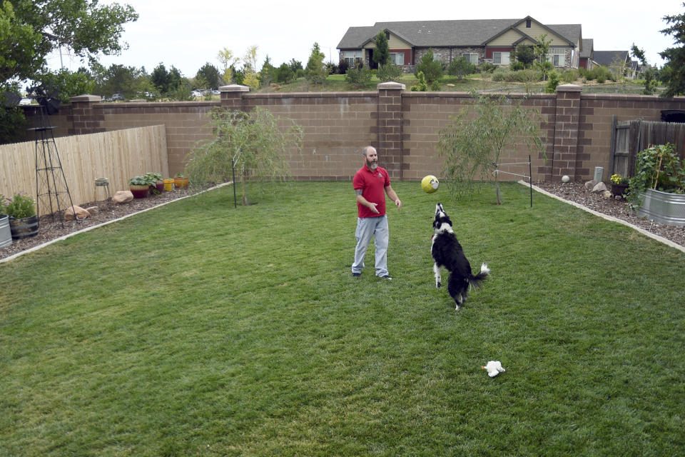 Kyle Tomcak plays with one of his dogs in the backyard of his house in Aurora, Colo., on Monday, July 18, 2022. Tomcak was in the market for a home priced around $450,000 for his in-laws and he and his wife bid on every house they toured, regardless of whether they fell in love with the home. He said his search became increasingly dispiriting as he not only lost out to investors fronting cash offers $100,000 over asking price but as mortgage rates started to balloon. He has since pulled out of the housing search. (AP Photo/Thomas Peipert)