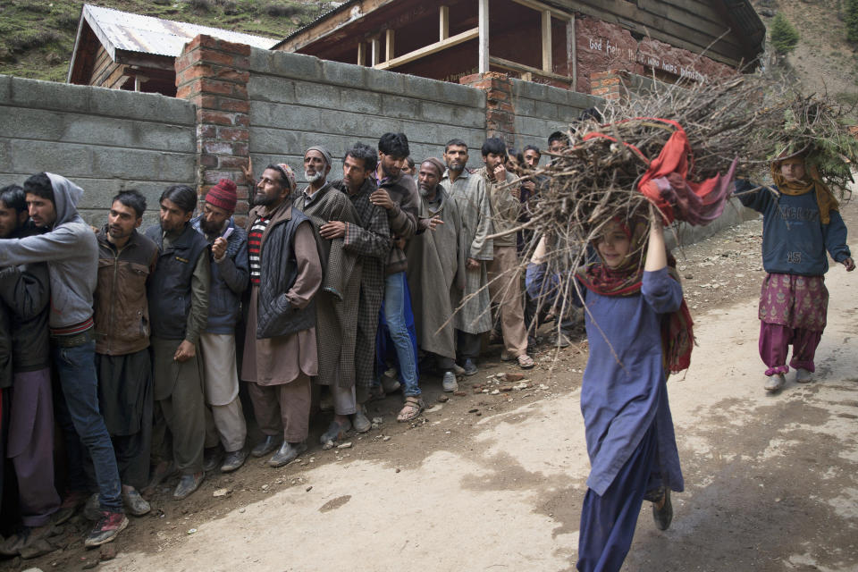 FILE - In this April 18, 2019, file photo, young Kashmiri girls carry firewood past voters queueing outside a polling station during the second phase of India's general elections, in Baba Nagri, about 44 kms. (28 miles) northeast of Srinagar, Indian controlled Kashmir. In the world’s largest democracy, few issues reach as broad a consensus as Kashmir, that the Muslim-majority region must remain part of Hindu-majority India. Modi is using this, and a February attack on Indian paramilitary forces in Kashmir, to consolidate the Hindu vote in India’s five-week elections that conclude May 21 to bolster his campaign-slogan claim to be India’s chowkidar, or watchman. (AP Photo/ Dar Yasin, File)