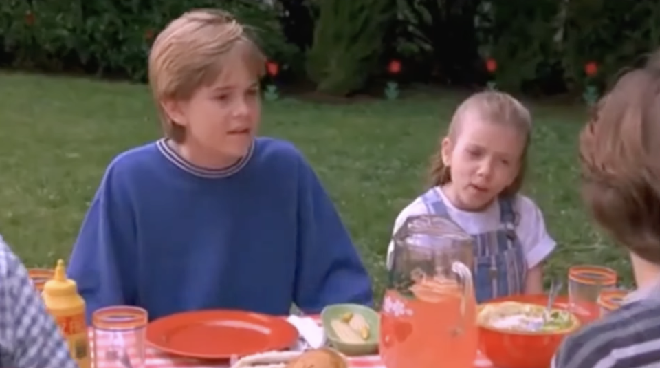 A screenshot of Scarlett Johansson as a kid, sitting at a picnic table with two boys