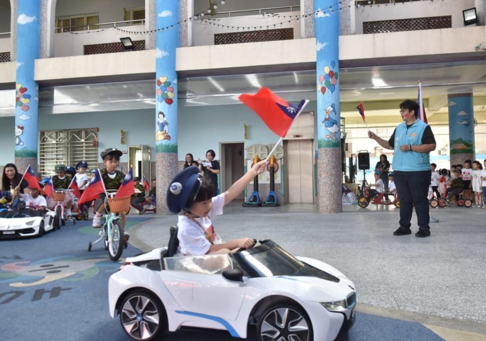 花蓮市幼在校內辦理閱兵大典，小朋友們有模有樣地入場，揮舞國旗跟市長魏嘉彥打招呼。(花蓮市公所提供)