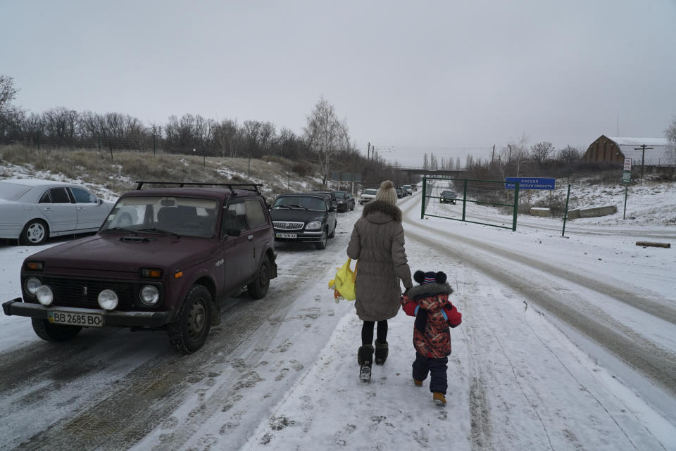 A Ukrainian woman with her child crosses the border from Ukrainian side of the Ukraine - Russia border to Russia in Milove town, eastern Ukraine, Sunday, Dec. 2, 2018. On a map, Chertkovo and Milove are one village, crossed by Friendship of Peoples Street which got its name under the Soviet Union and on the streets in both places, people speak a mix of Russian and Ukrainian without turning choice of language into a political statement.(AP Photo/Evgeniy Maloletka)